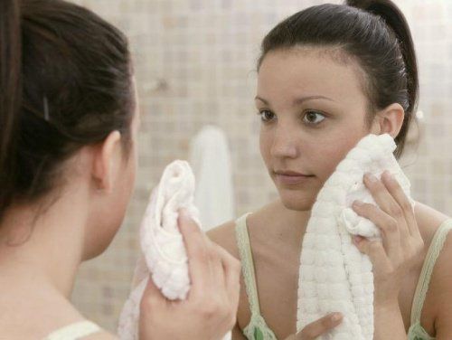 Женщина вытирает лицо полотенцем перед зеркалом