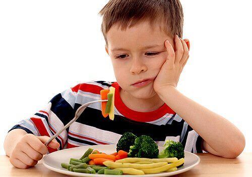 Мальчик смотрит на овощи с отвращением.