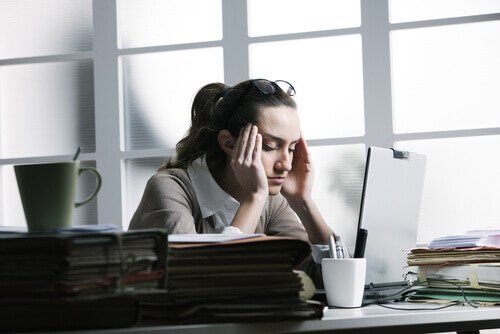Женщина в офисе страдает от головной боли, вызванной чрезмерным стрессом