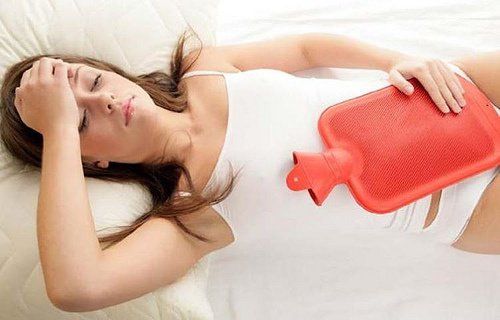 Лежащая женщина на кровати с бутылкой с горячей водой, менструация
