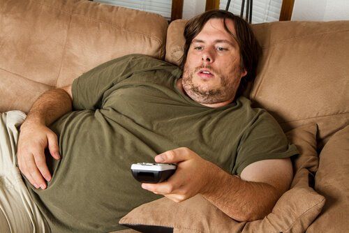 Тучный мужчина сидит на диване перед телевизором и сердцебиение